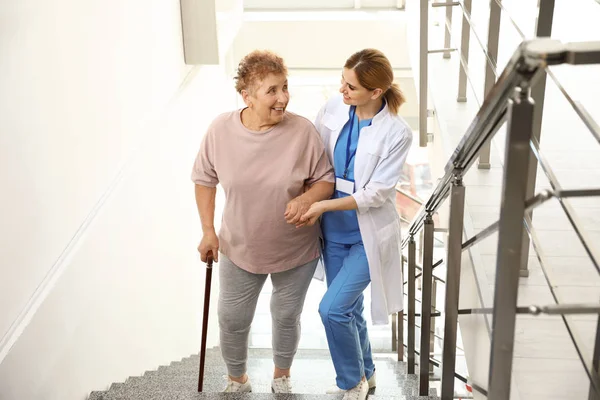 Nurse assisting elderly woman on stairs indoors