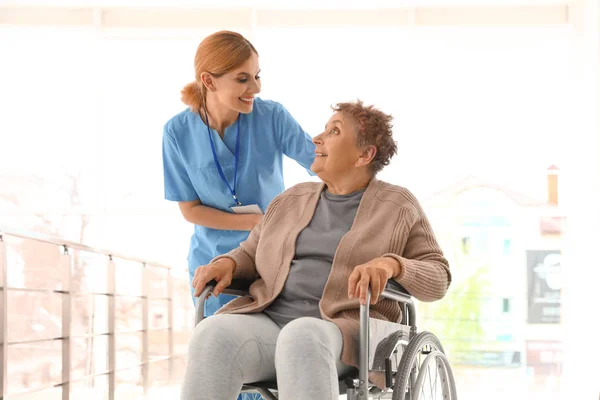 Enfermeira assistindo a mulher idosa em cadeira de rodas dentro de casa — Fotografia de Stock