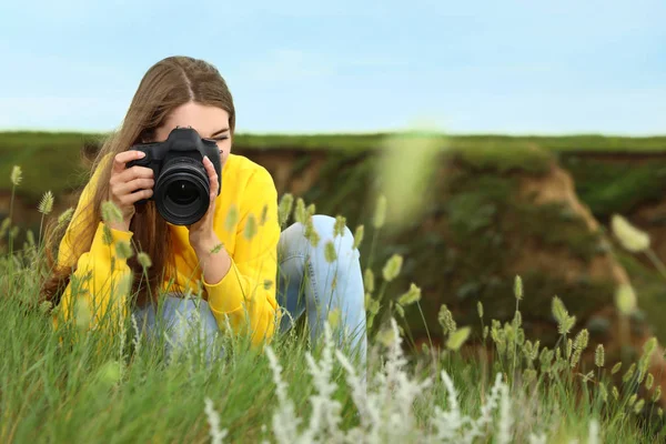 Kobieta fotografa biorąc obraz pięknych roślin z profesjonalnym aparatem na zielonym wzgórzu — Zdjęcie stockowe