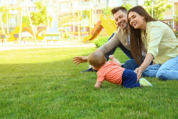 Föräldrar hjälpa sina bedårande lilla barnet att krypa utomhus. Utrymme för text — Stockfoto