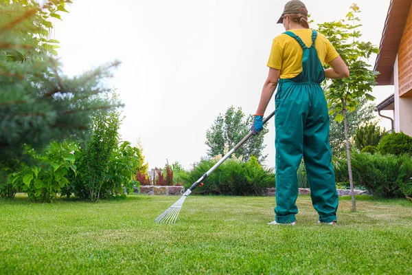 Woman raking green lawn at backyard outdoors. Home gardening — Stock Photo, Image