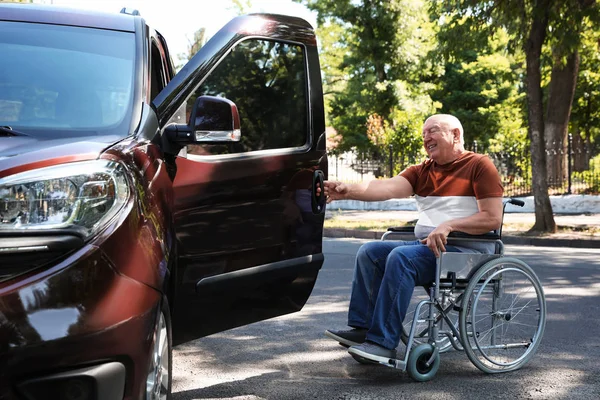 Senior man in wheelchair opening door of his van outdoors