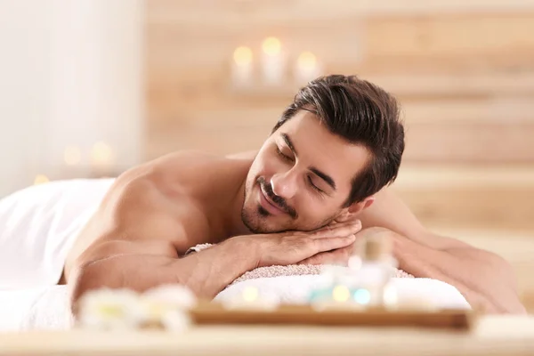 Schöner junger Mann entspannt sich auf Massagetisch im Wellness-Salon — Stockfoto
