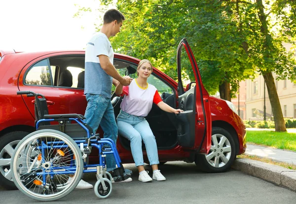 장애인 여성이 차에서 휠체어 야외로 나가도록 돕는 청년 — 스톡 사진