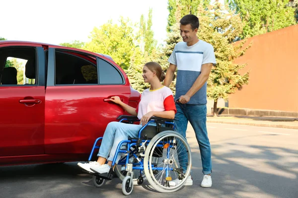 Молодий чоловік допомагає інвалідній жінці в інвалідному візку потрапити в машину на відкритому повітрі — стокове фото