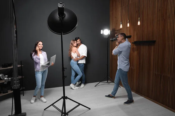 Fotógrafo profesional con asistente tomando fotos de pareja joven en estudio moderno — Foto de Stock