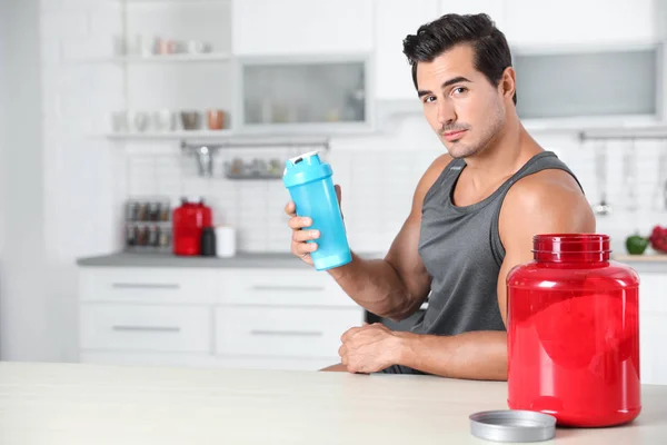 Homem atlético jovem com pó de batido de proteína na cozinha, espaço para texto — Fotografia de Stock