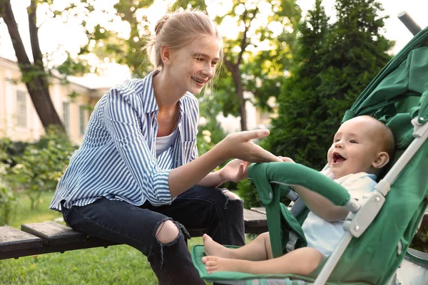 Tiener nanny met schattig baby in kinderwagen spelen in park — Stockfoto