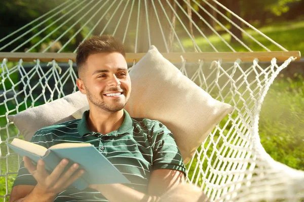 Młody człowiek czytanie książka w wygodny hamak w zielony ogród — Zdjęcie stockowe