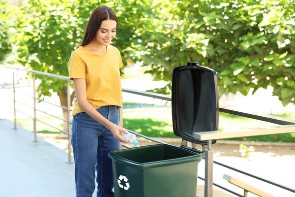 Νεαρή γυναίκα που ρίχνει πλαστικό μπουκάλι στον κάδο ανακύκλωσης σε εξωτερικούς χώρους — Φωτογραφία Αρχείου