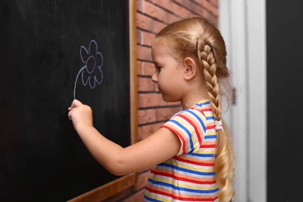 Söt liten vänsterhänt flicka ritning på svarta tavlan nära tegelvägg — Stockfoto