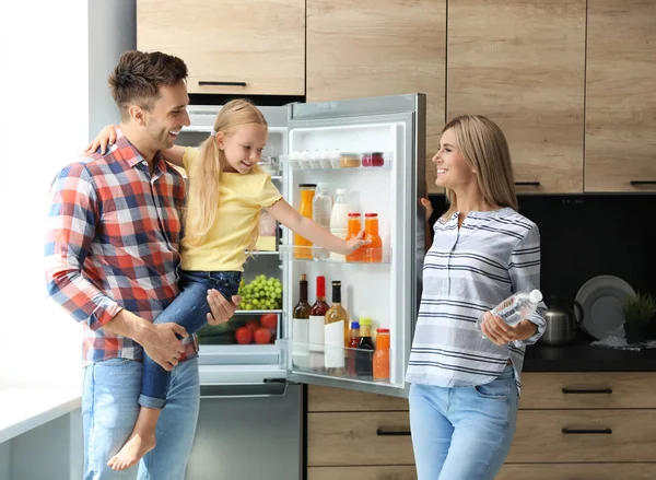 Família feliz com garrafa de água perto da geladeira na cozinha — Fotografia de Stock