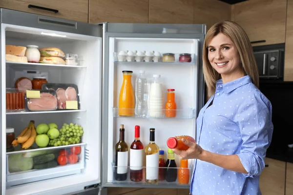 Nő üveg lé közelében hűtőszekrény a konyhában — Stock Fotó