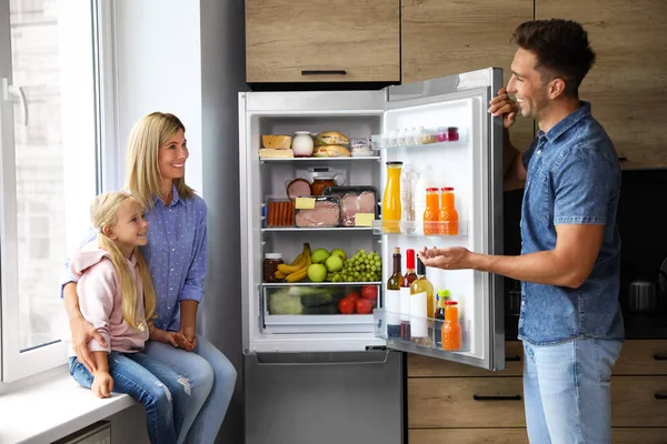 Família feliz perto do refrigerador cheio de produtos na cozinha — Fotografia de Stock