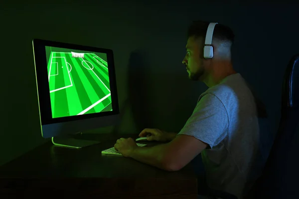 Человек в наушниках играет в видеоигры на современном компьютере в темной комнате — стоковое фото