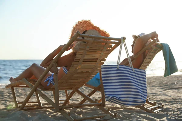 Pareja joven relajándose en tumbonas en la playa cerca del mar — Foto de Stock