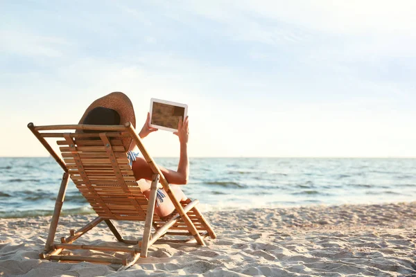 Fiatal nő tabletta pihen a nyugágyon a strandon — Stock Fotó