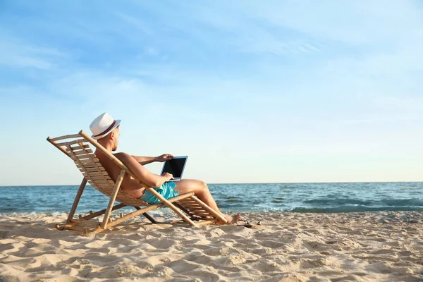 Jonge man met laptop in terrasstoel op het strand — Stockfoto