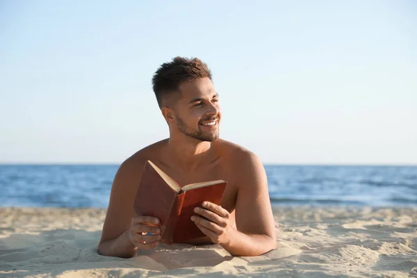 Joven leyendo libro sobre playa de arena cerca del mar — Foto de Stock