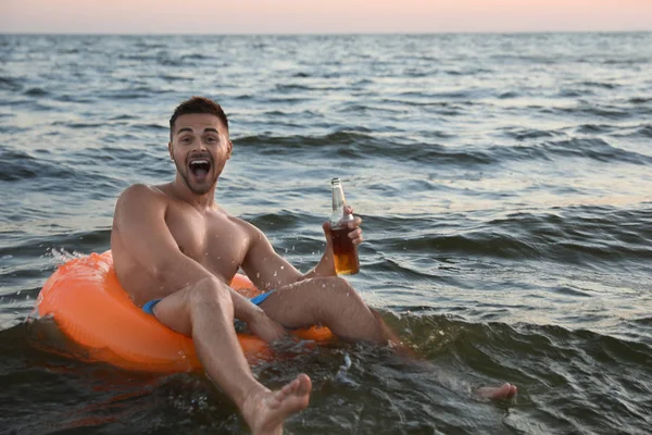 Pria muda yang bahagia dengan minuman di atas cincin tiup dalam air — Stok Foto