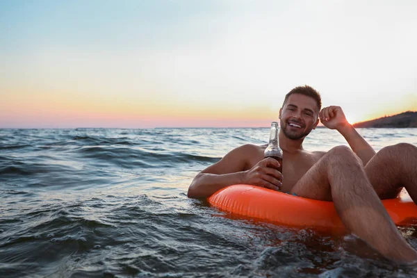 Happy young man with drink on inflatable ring in water