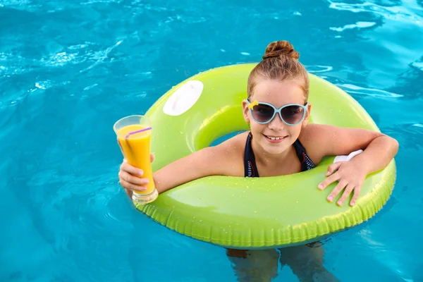 Menina pequena feliz com anel inflável e bebida na piscina — Fotografia de Stock