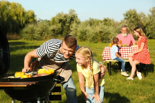 Tată cu o fetiță la grătar și familia lor în parc — Fotografie, imagine de stoc