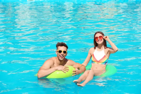 Feliz pareja joven con anillos inflables en la piscina — Foto de Stock