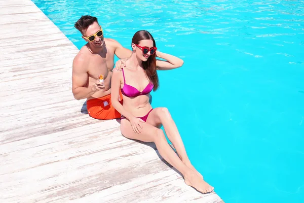 Hombre joven aplicando crema de protección solar a su novia en la piscina — Foto de Stock