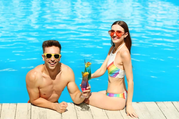Happy young couple with cocktails resting at swimming pool — Stock Photo, Image