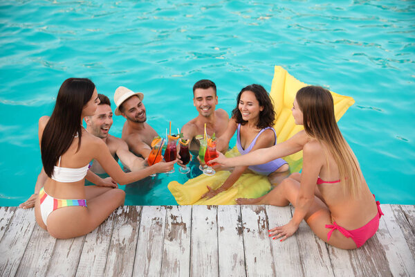 Счастливые молодые друзья с освежающими коктейлями, наслаждающиеся вечеринкой в бассейне
