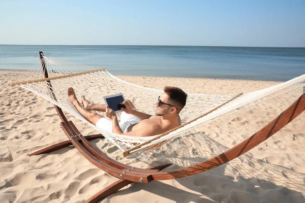 Giovane con tablet in amaca sulla spiaggia — Foto Stock