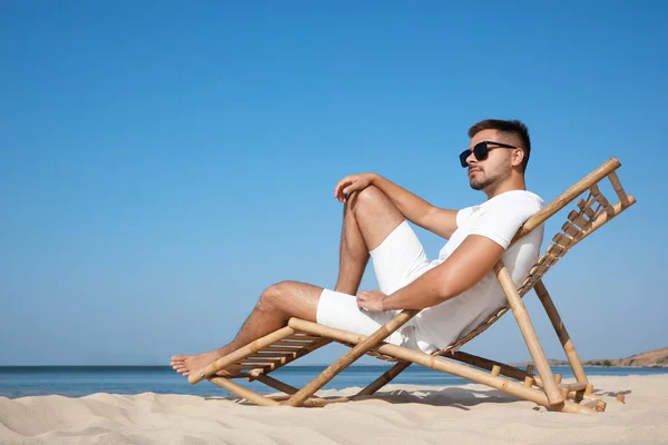 Hombre joven relajándose en la silla de cubierta en la playa de arena — Foto de Stock