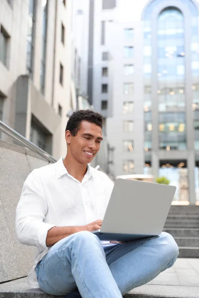 Handsome young African-American man with laptop sitting on stairs outdoors Royalty Free Stock Photos