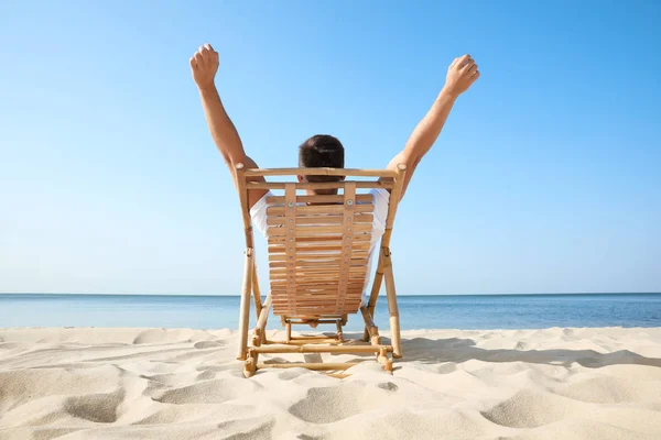 Young man relaxing in deck chair on sandy beach — Stock Photo, Image