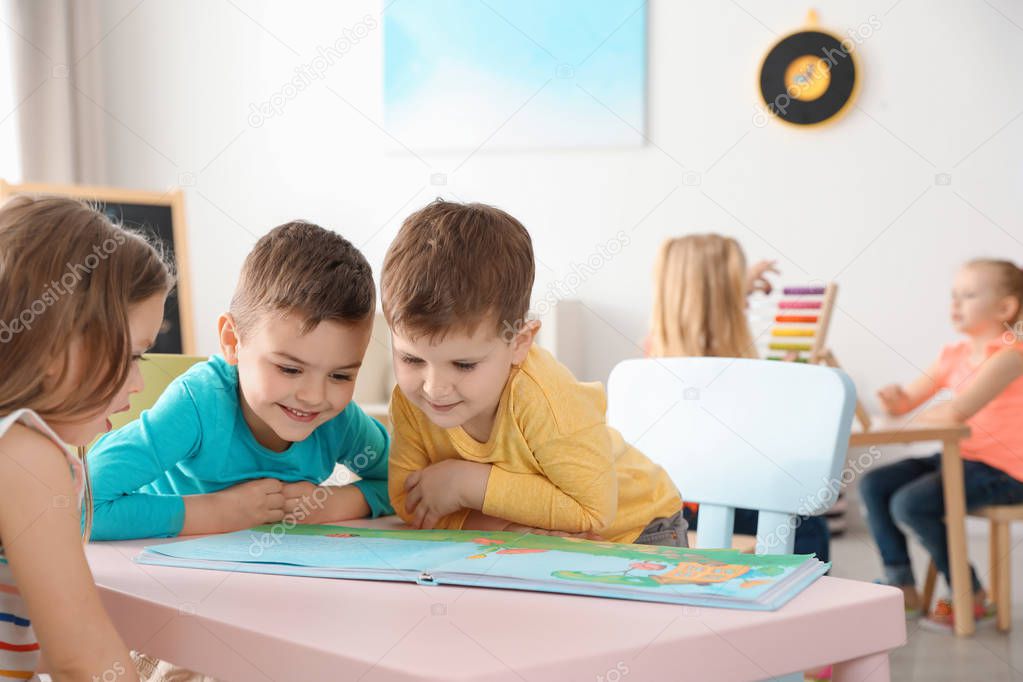 Cute little children reading book at table indoors. Learning and playing