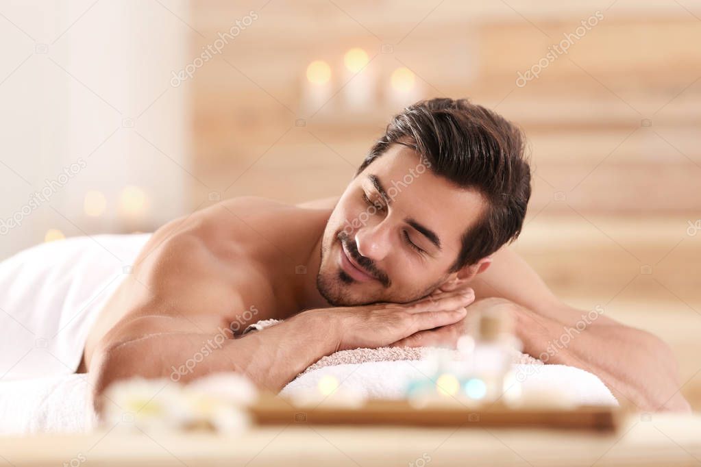 Handsome young man relaxing on massage table in spa salon