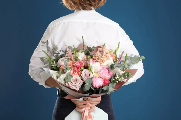 Man hiding beautiful flower bouquet behind his back on blue background