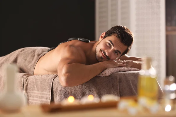 Handsome young man receiving hot stone massage in spa salon — Stock Photo, Image