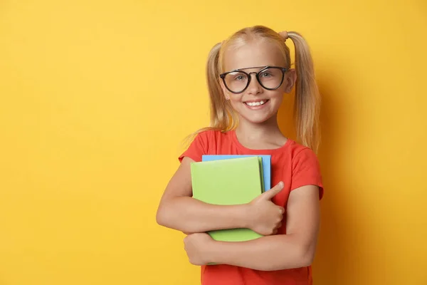 Linda niña con gafas y libros sobre fondo amarillo. Concepto de lectura — Foto de Stock