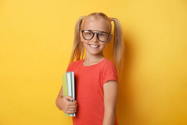 Linda niña con gafas y libros sobre fondo amarillo. Concepto de lectura — Foto de Stock