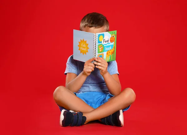 Mignon petit garçon lecture livre sur fond rouge — Photo