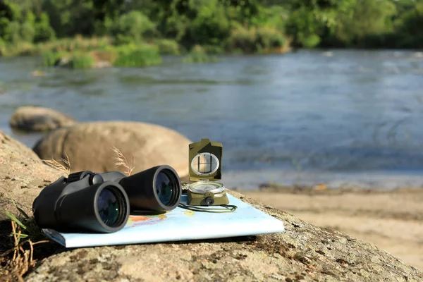 双眼鏡、コンパス、川の近くの石の上に地図、テキストのためのスペース。キャンプ用品 — ストック写真