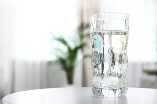 Glass of water on table in room, space for text. Refreshing drink