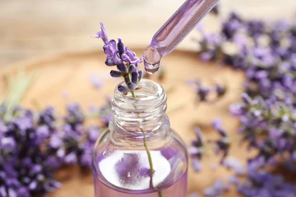 Natural oil dripping into bottle and lavender flowers on table, closeup. Cosmetic product