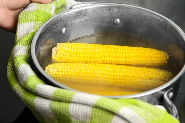 Person holding pot with boiled corns in hot water on stove, closeup — Stock Photo, Image