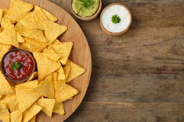 Mexican nacho chips with different sauces on wooden background, flat lay. Space for text — Stock Photo, Image