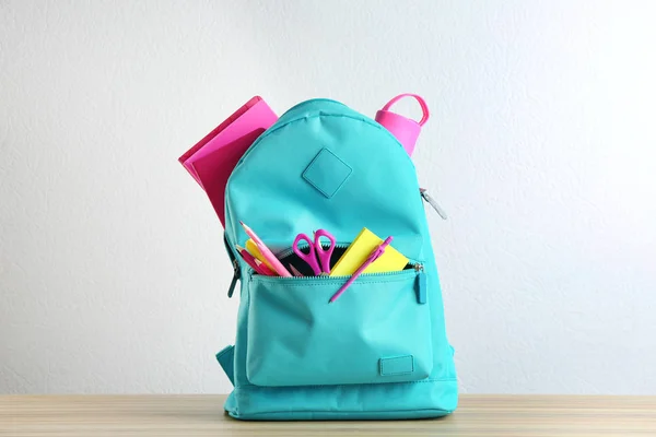 Heller Rucksack mit verschiedenen Schulschreibwaren auf Holztisch vor weißem Hintergrund — Stockfoto