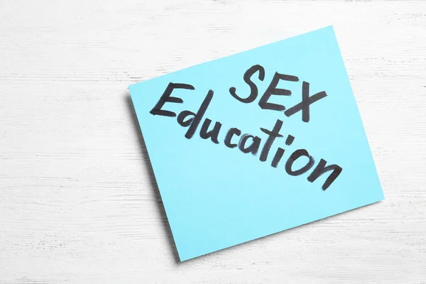 Nota com a frase "SEX EDUCATION" em fundo de madeira branco, vista superior — Fotografia de Stock