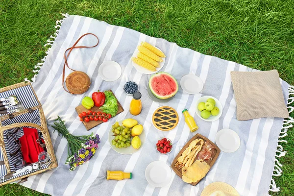 Picknickdecke mit leckeren Snacks auf Gras im Park — Stockfoto